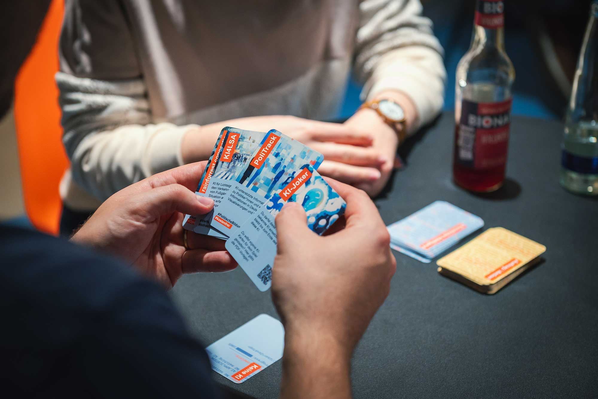 Blick auf die Hände einer Person, die Spielkarten des Kartenspieles "KI-Kompass" in der Hand hält.